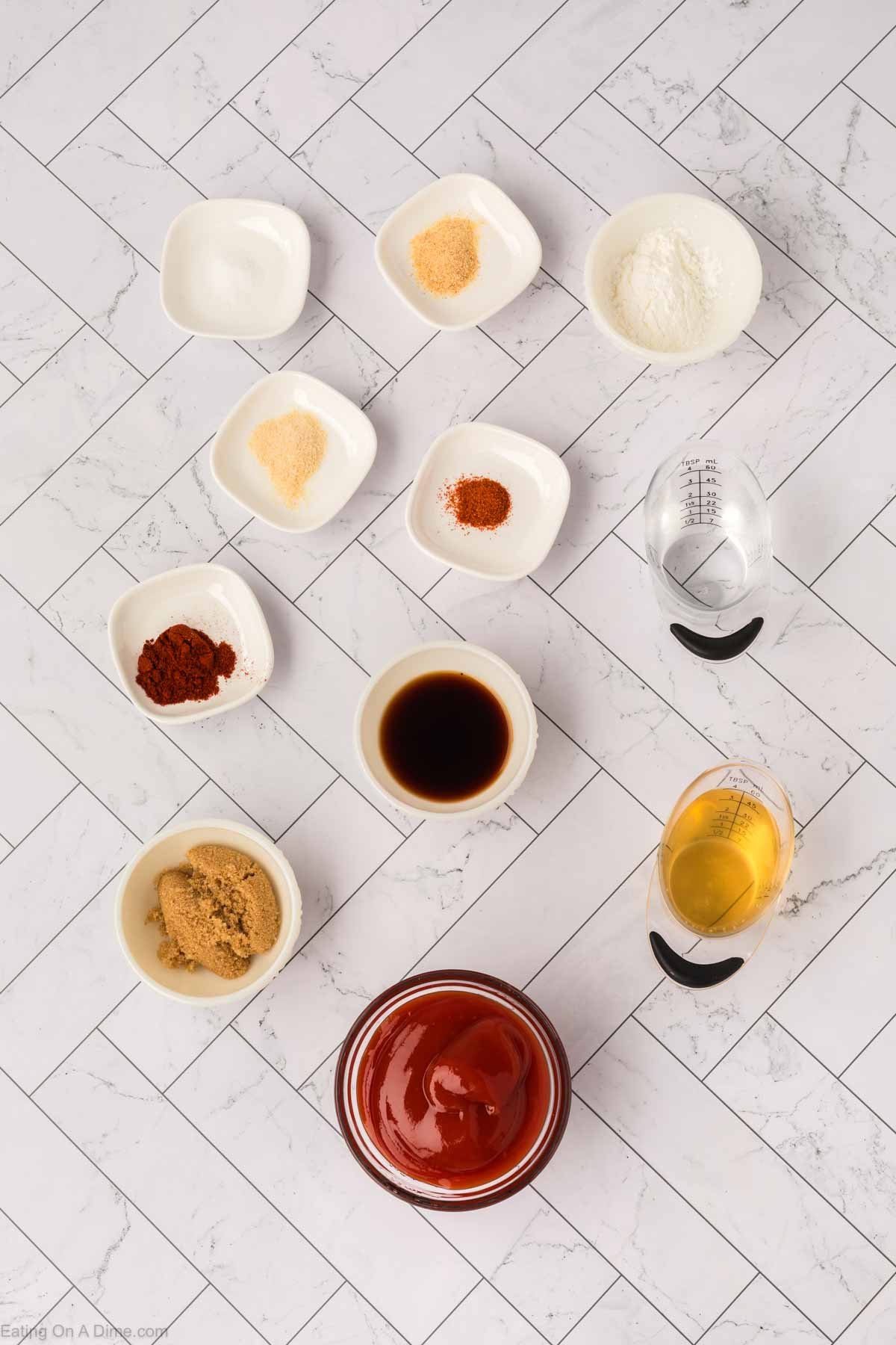 An overhead view of small bowls and measuring cups with ingredients for Arby’s Sauce, including ketchup, brown sugar, seasonings, soy sauce, and liquids, arranged neatly on a white tiled surface—perfect for recreating the classic Arby’s Sauce recipe at home.