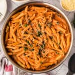 A skillet filled with Creamy Tomato Basil Pasta—penne in a rich tomato sauce, garnished with chopped basil and grated cheese—sits on a marble countertop.