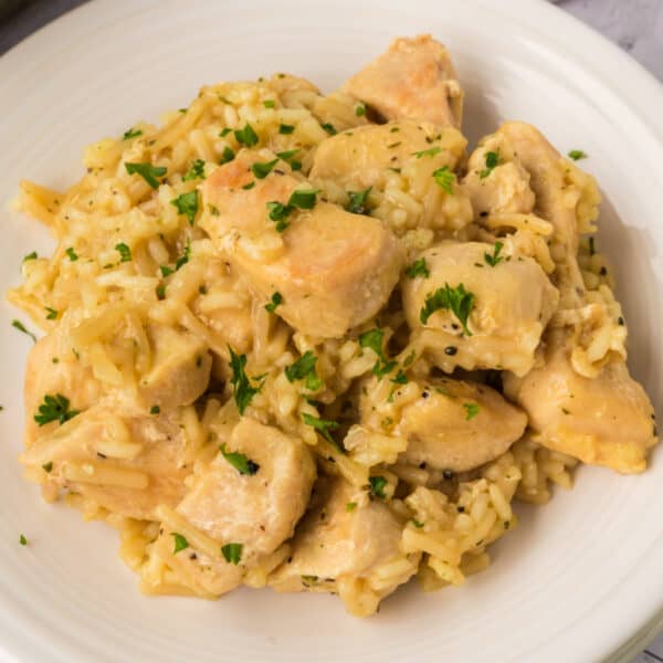 A white plate filled with creamy Rice A Roni Chicken Casserole, garnished with chopped parsley. The dish features chunks of cooked chicken mixed with seasoned rice for a comforting meal.