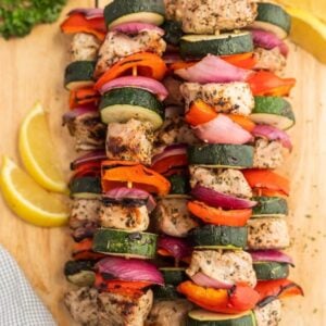 Colorful grilled skewers with chicken, zucchini, red onion, and bell pepper are arranged on a wooden board with lemon wedgesโperfect for adding variety to your Meal Plan 89 or inspiring fresh ideas for meal planning.
