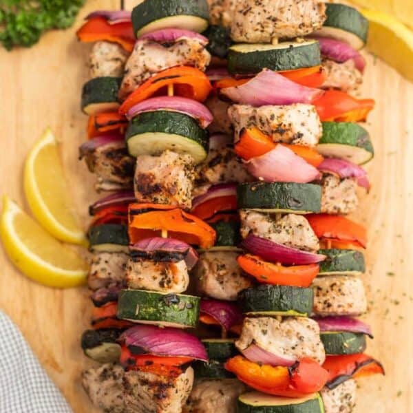 Colorful grilled skewers with chicken, zucchini, red onion, and bell pepper are arranged on a wooden board with lemon wedges—perfect for adding variety to your Meal Plan 89 or inspiring fresh ideas for meal planning.