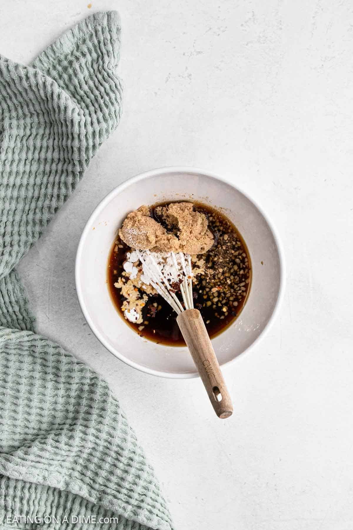 A white bowl containing brown sugar, soy sauce, and other ingredients for a marinade.