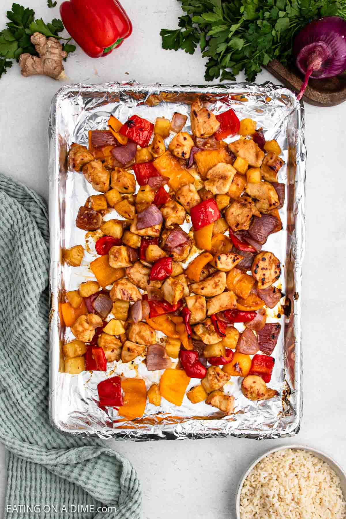 Sheet pan lined with foil holds roasted Sheet Pan Chicken pieces, red and yellow bell peppers, and red onions.