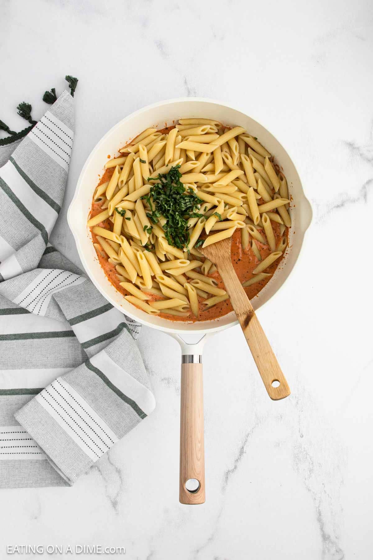 A white skillet filled creamy tomato sauce, and fresh chopped herbs with a wooden spoon.