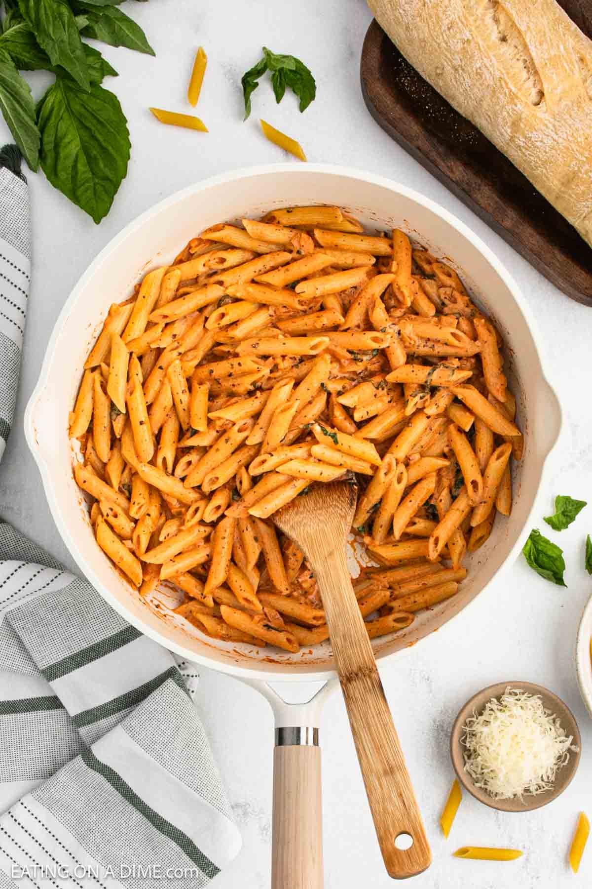 A white skillet filled with pasta mixed in a creamy tomato base sauce with a wooden spoon.