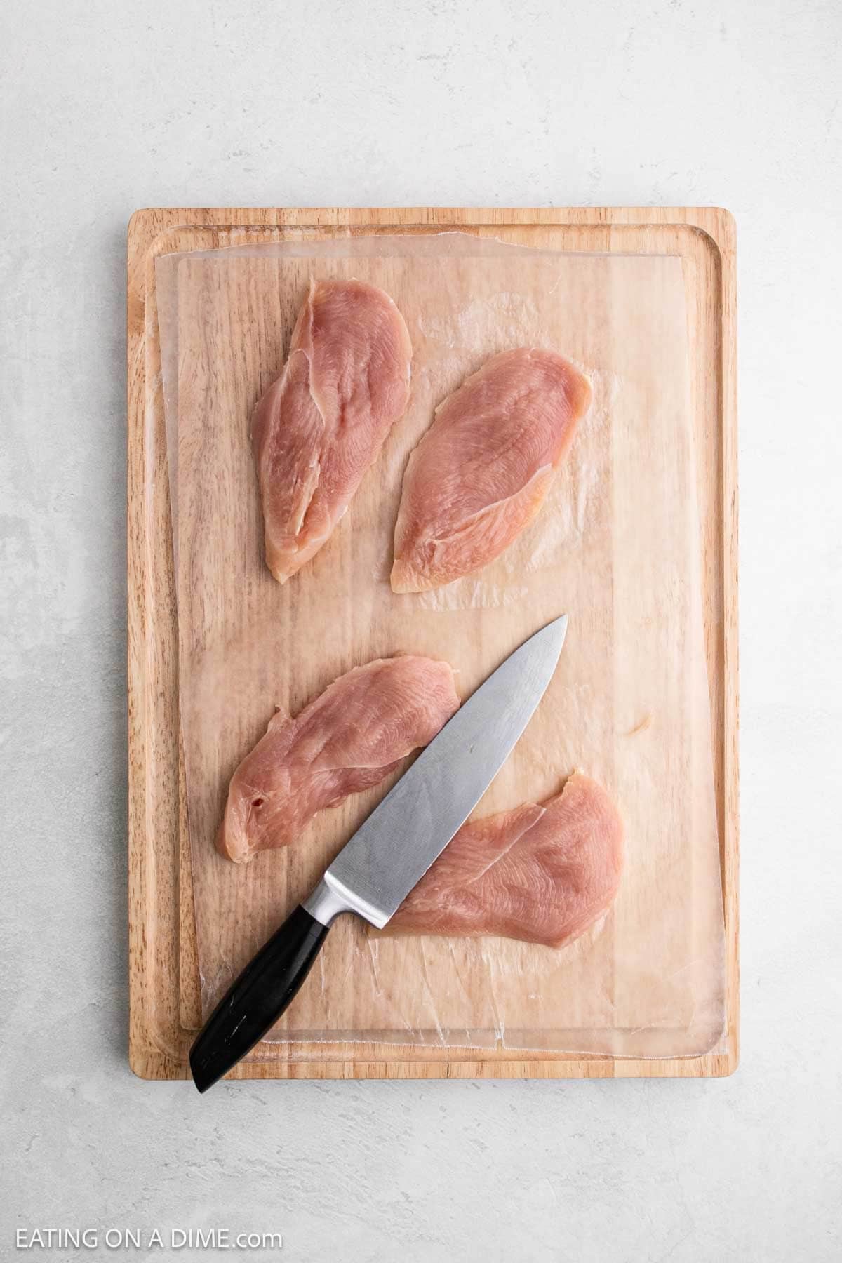 Raw chicken cutlets on a wooden cutting board with a kitchen knife placed on top, ready for preparation.