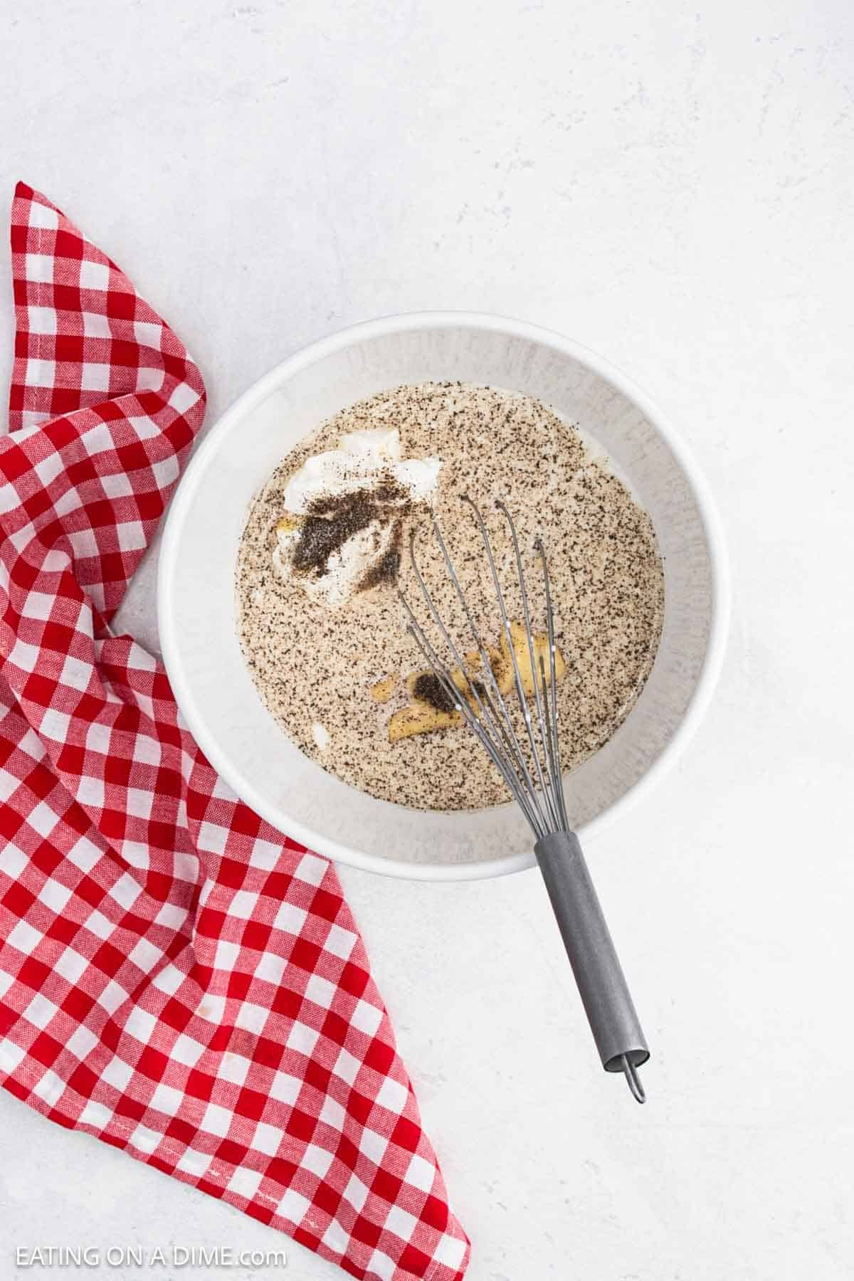 Whisking together chicken soup, sour cream, milk, and spices in a bowl.