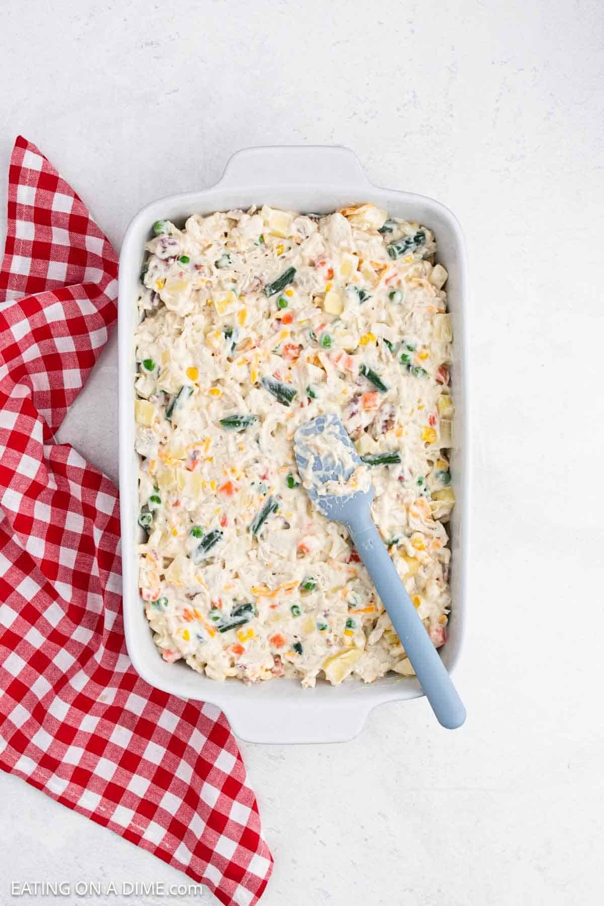 Spreading the casserole mixture into a baking dish with a blue spatula.