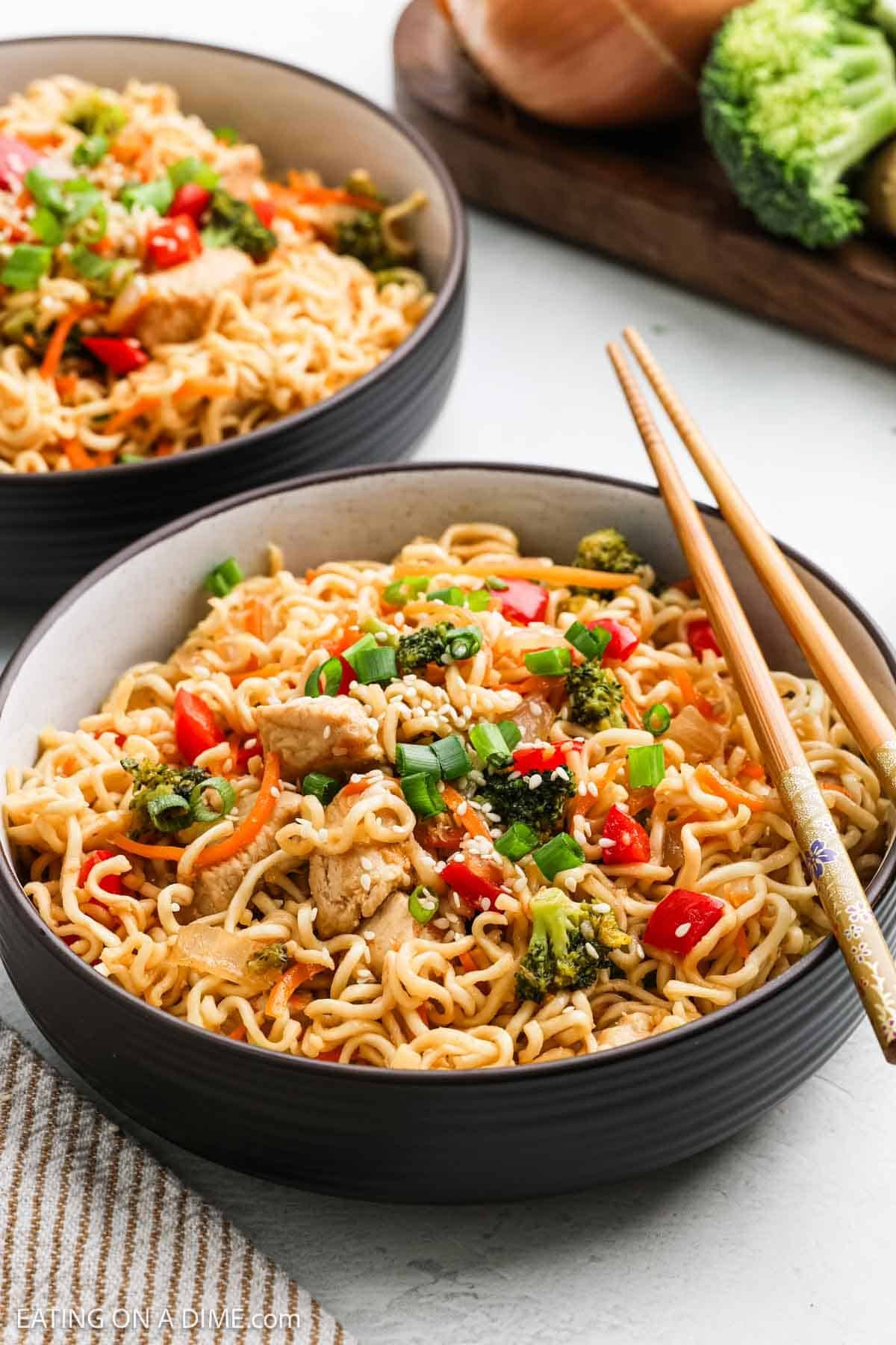 Two bowls of Chicken Ramen topped with broccoli, red bell peppers, and green onions, along with tender pieces of chicken. The bowls sit on a white surface, with a pair of chopsticks resting on one for an inviting touch.