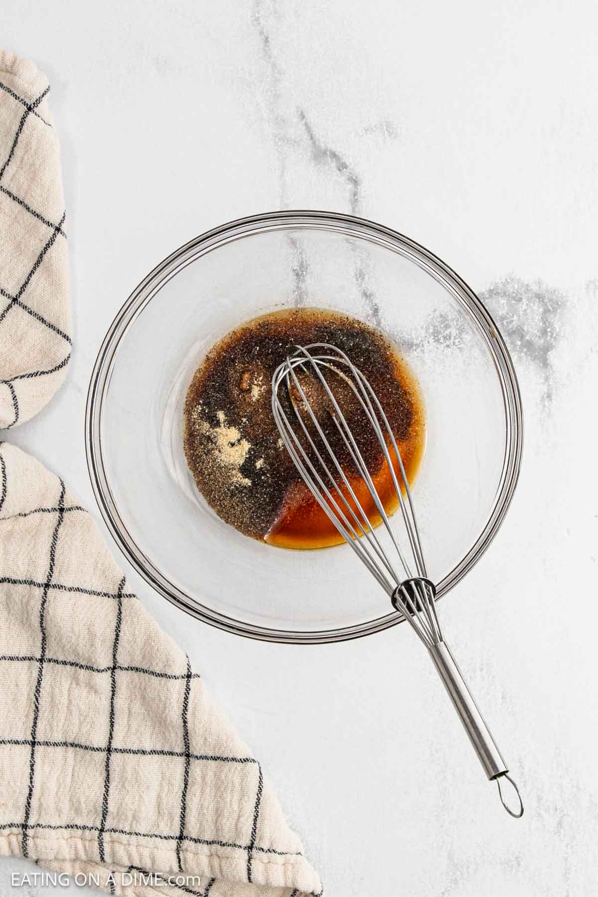 In a mixing bowl, there is a whisk with soy sauce, sesame oil, onion powder, pepper and salt.