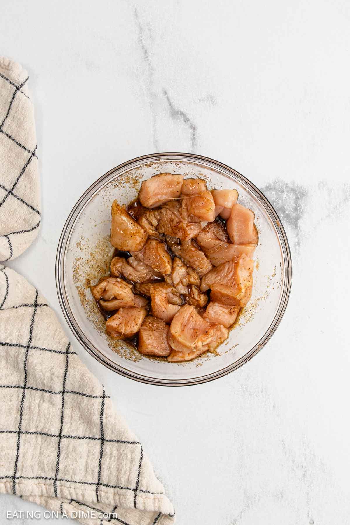 A glass bowl filled with marinated raw Chicken pieces sits