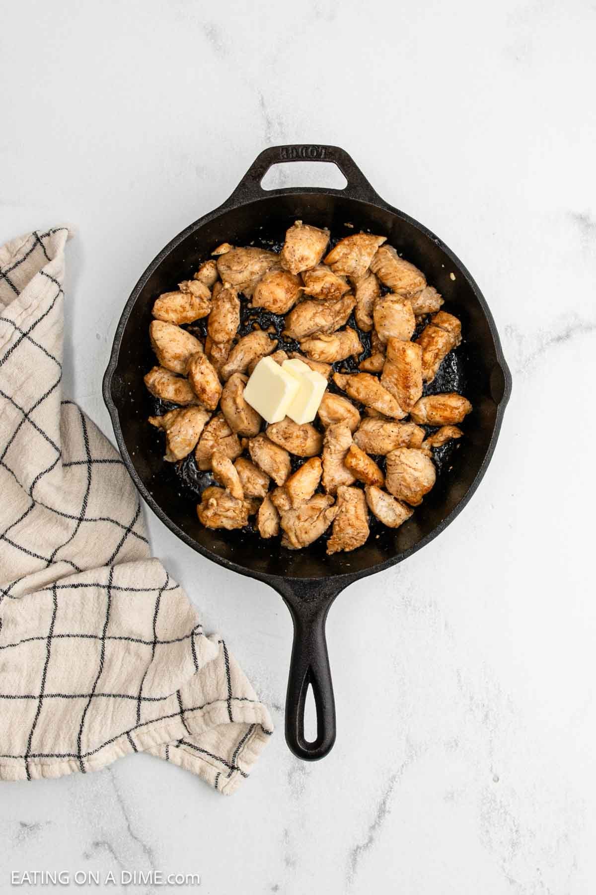 A cast iron skillet filled with browned pieces of Hibachi Chicken and two pats of butter in the center,