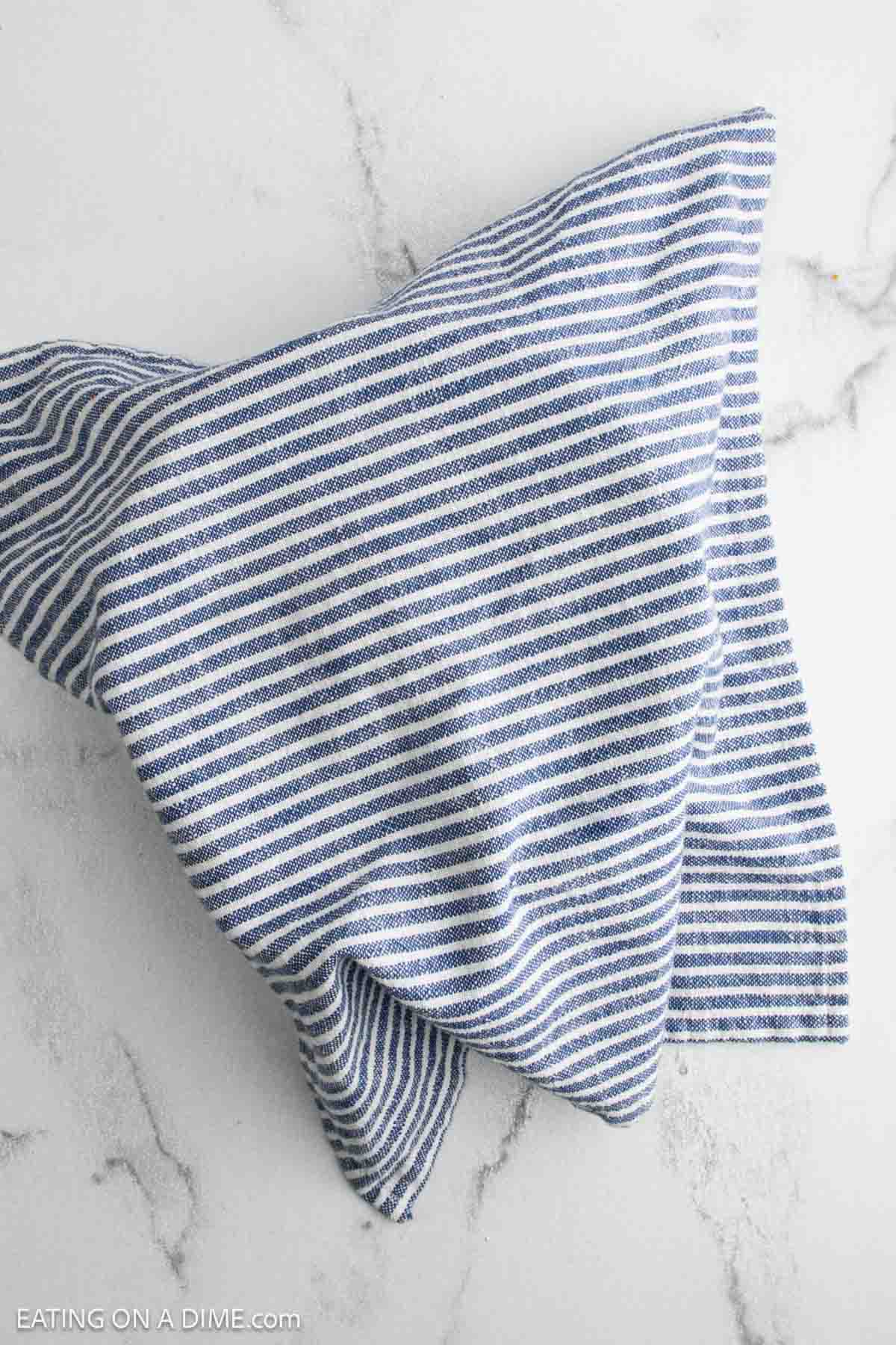 A blue and white striped cloth towel, perfect for cooling sourdough bread or cheddar jalapeño loaves, is spread out and slightly folded on a light marble surface.