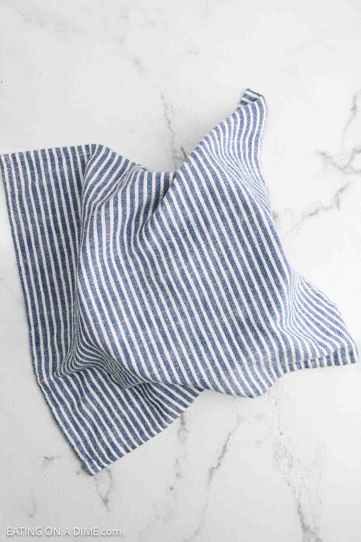 A blue and white striped kitchen towel is spread out on a light marble surface, ready to cradle a fresh loaf of jalapeño sourdough bread.