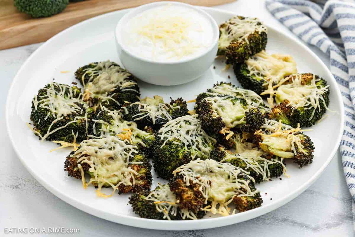 Smash broccoli on a white platter with a bowl of dipping sauce on the side.