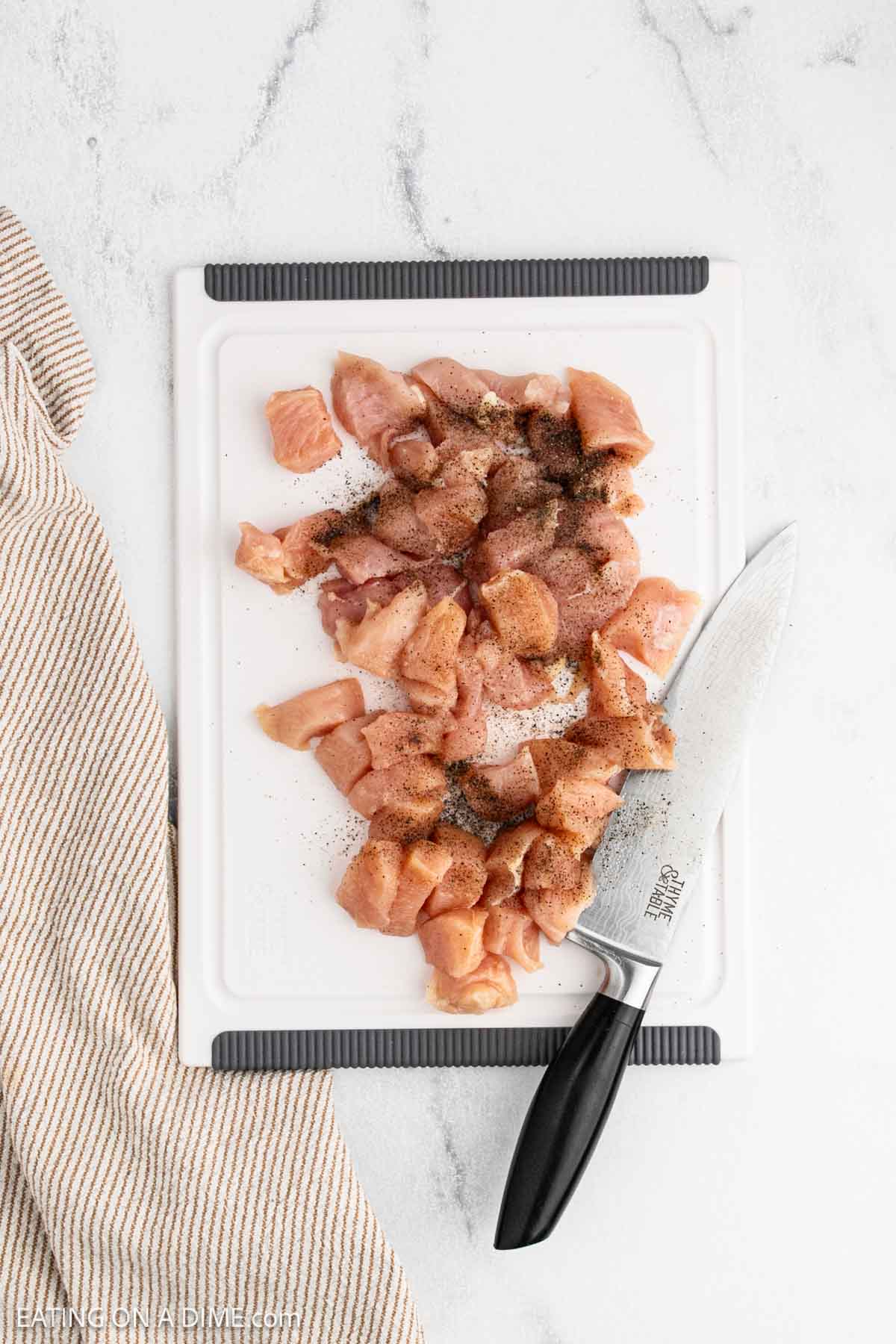 Diced raw chicken on a cutting board topped with salt and pepper.