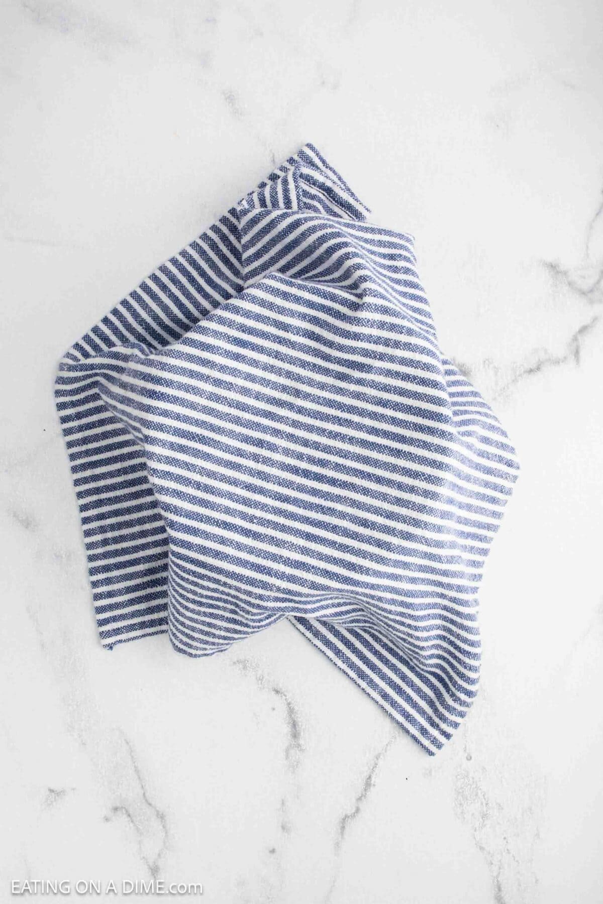 A blue and white striped kitchen towel is crumpled on a white marble surface, ready for your next sourdough recipe.