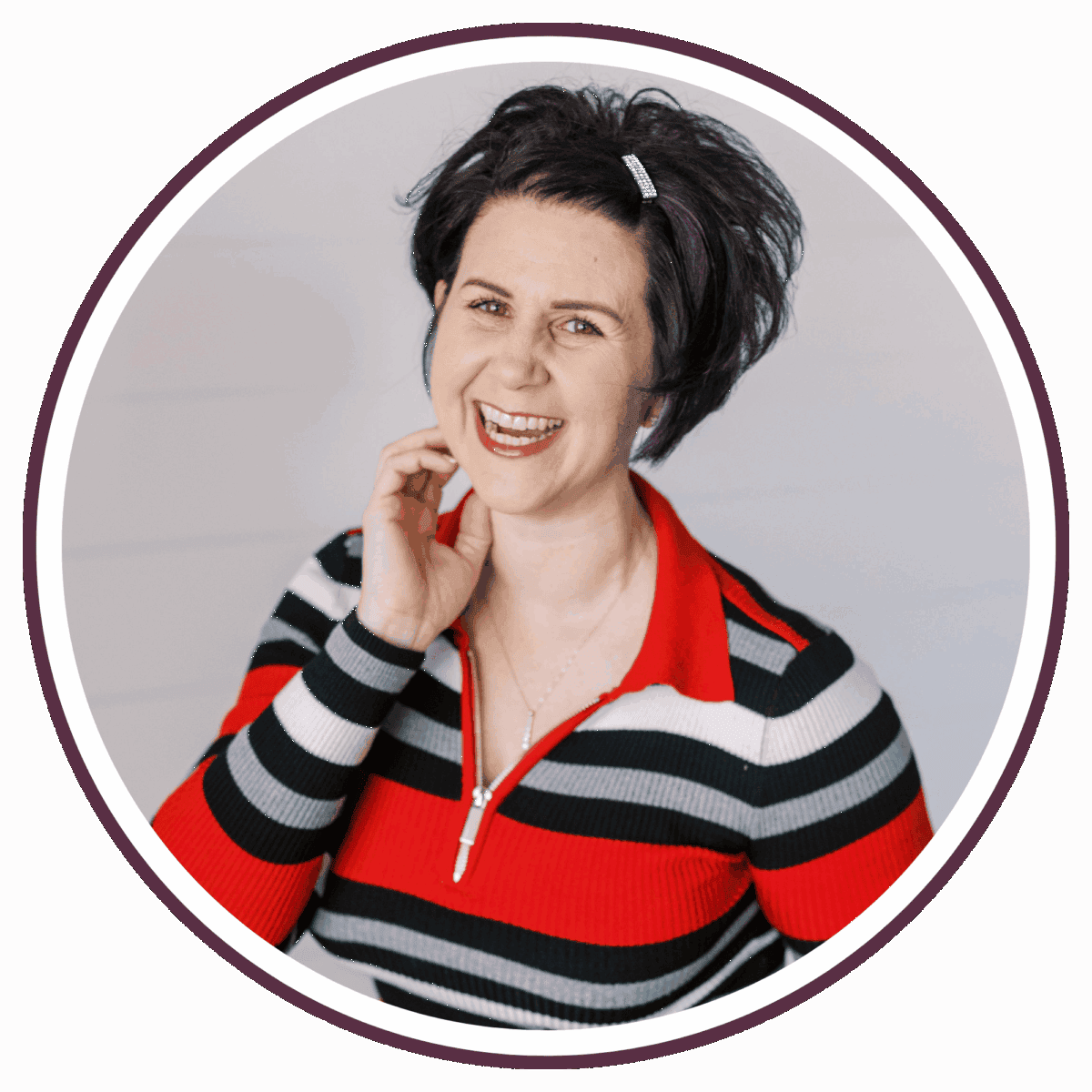 A woman with short dark hair, wearing a red, black, and white striped top, smiles warmly and touches her neck. She is framed by a circular border against a light backgroundโher style is reminiscent of Carrieโs effortless charm.