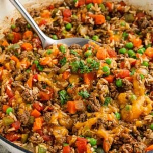 A close-up of a skillet filled with ground beef, rice, peas, diced tomatoes, carrots, green beans, onions, and melted cheddar cheese—an ideal Meal Plan 99 option—garnished with fresh parsley and a serving spoon in the pan.