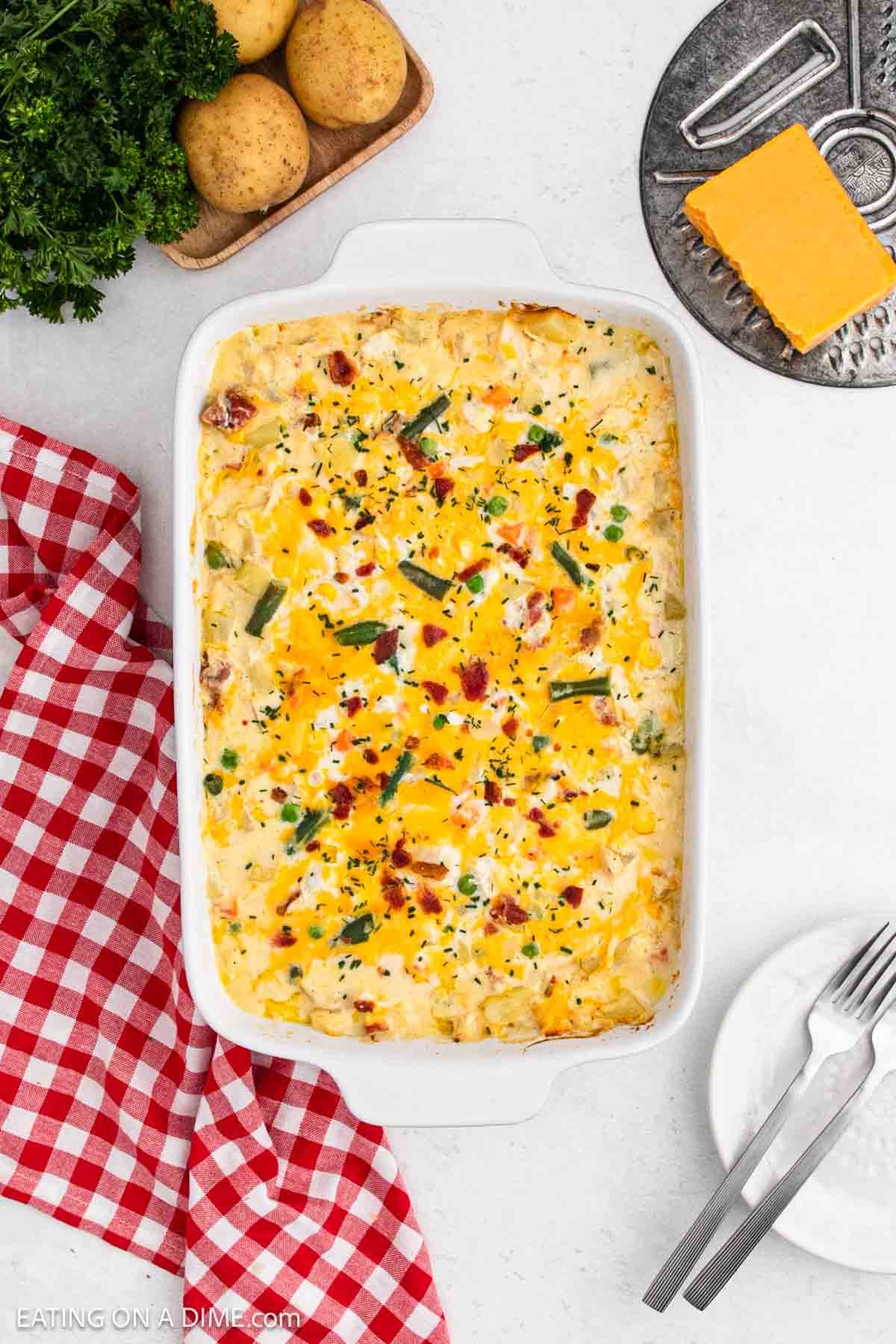Baked casserole in a baking dish with a block of cheese and whole potatoes on the side sitting on a platter.