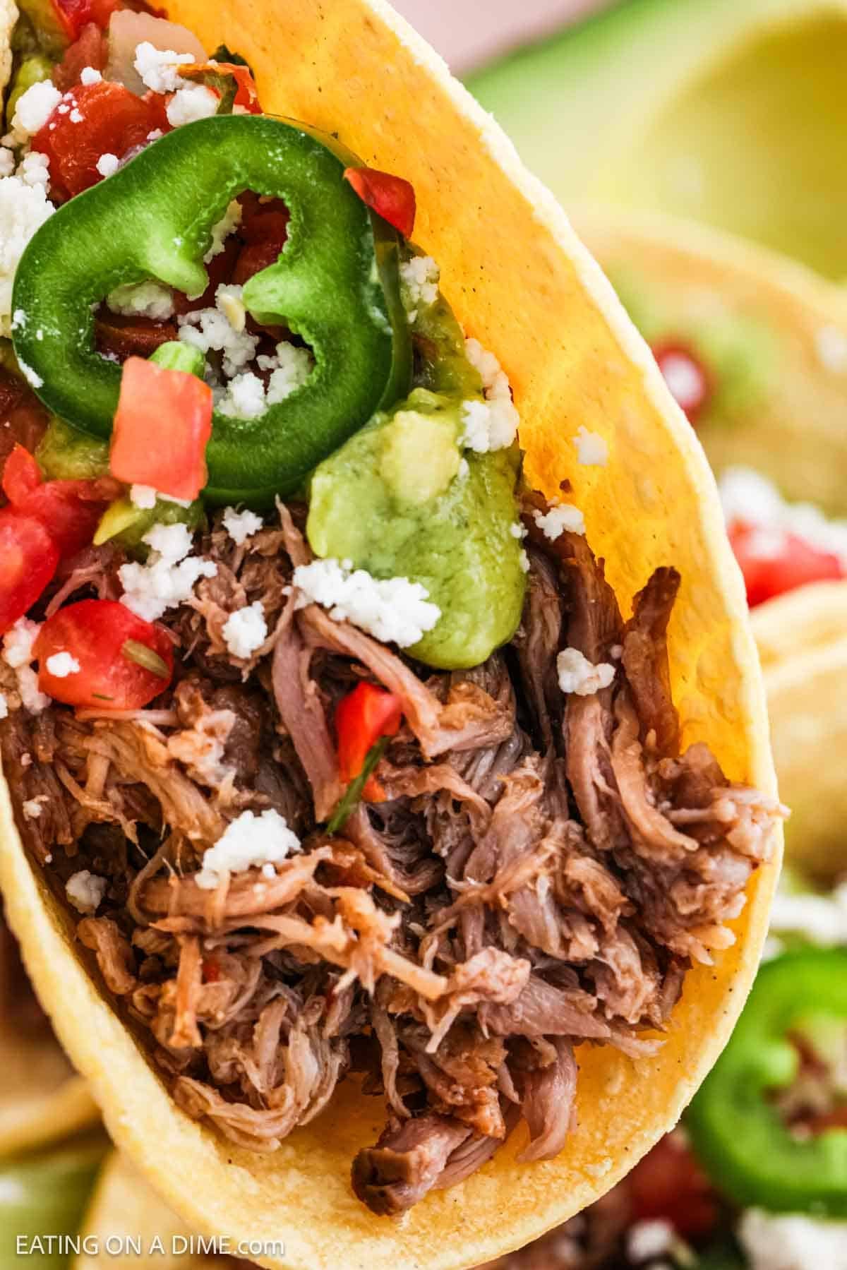 Close up image of shredded pork tacos topped with cheese crumbled, pico de gallo, and sliced jalapenos.