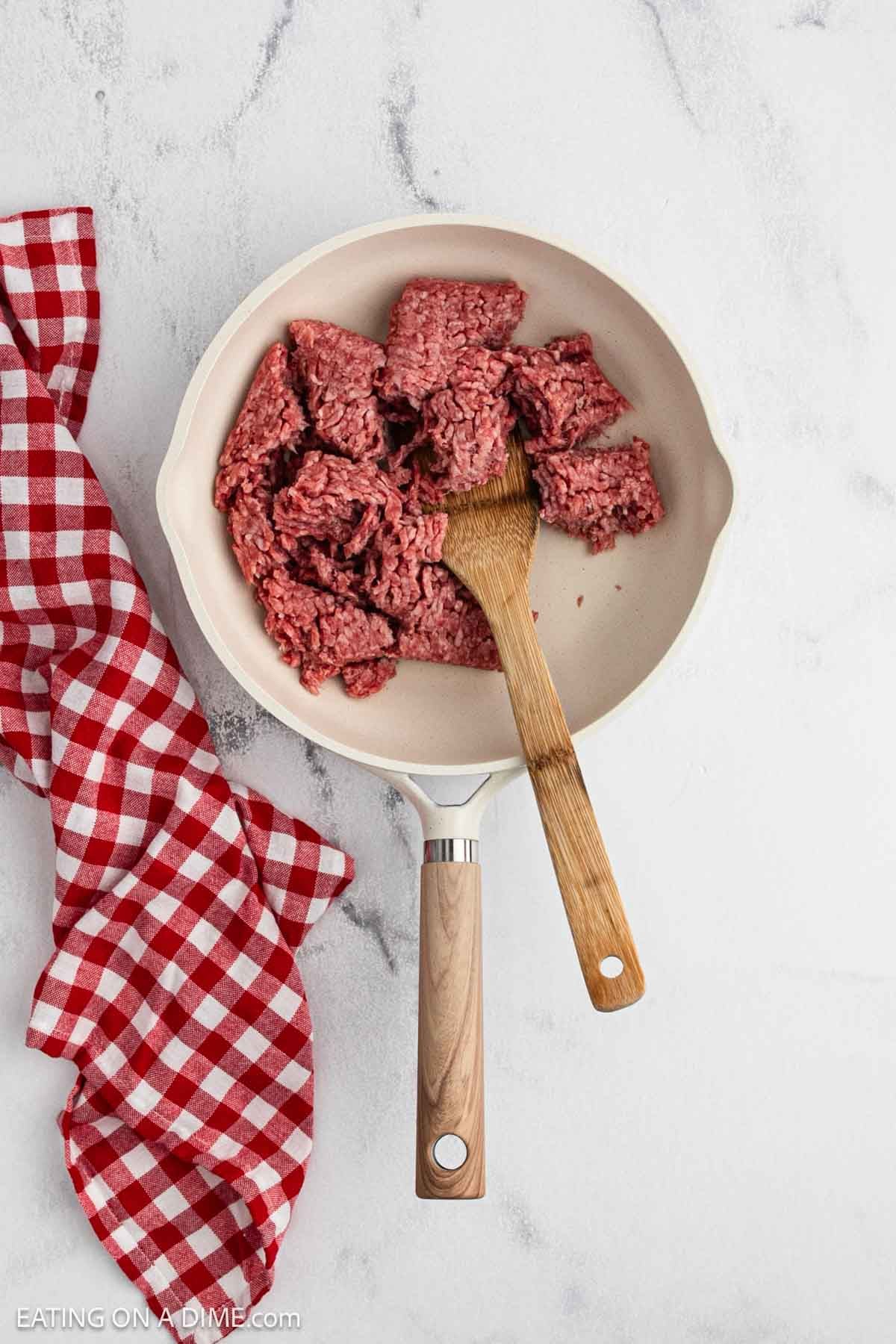 Cooking ground beef in a skillet with a wooden spoon.