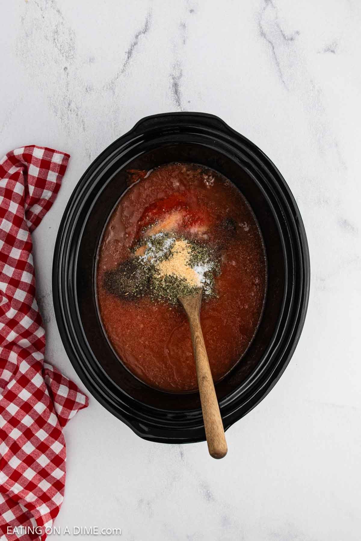 Sauce and spices in the crock pot with a wooden spoon.