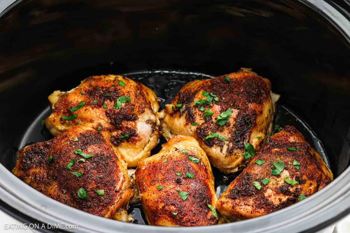 Golden brown chicken thighs in the slow cooker topped with chopped parsley.