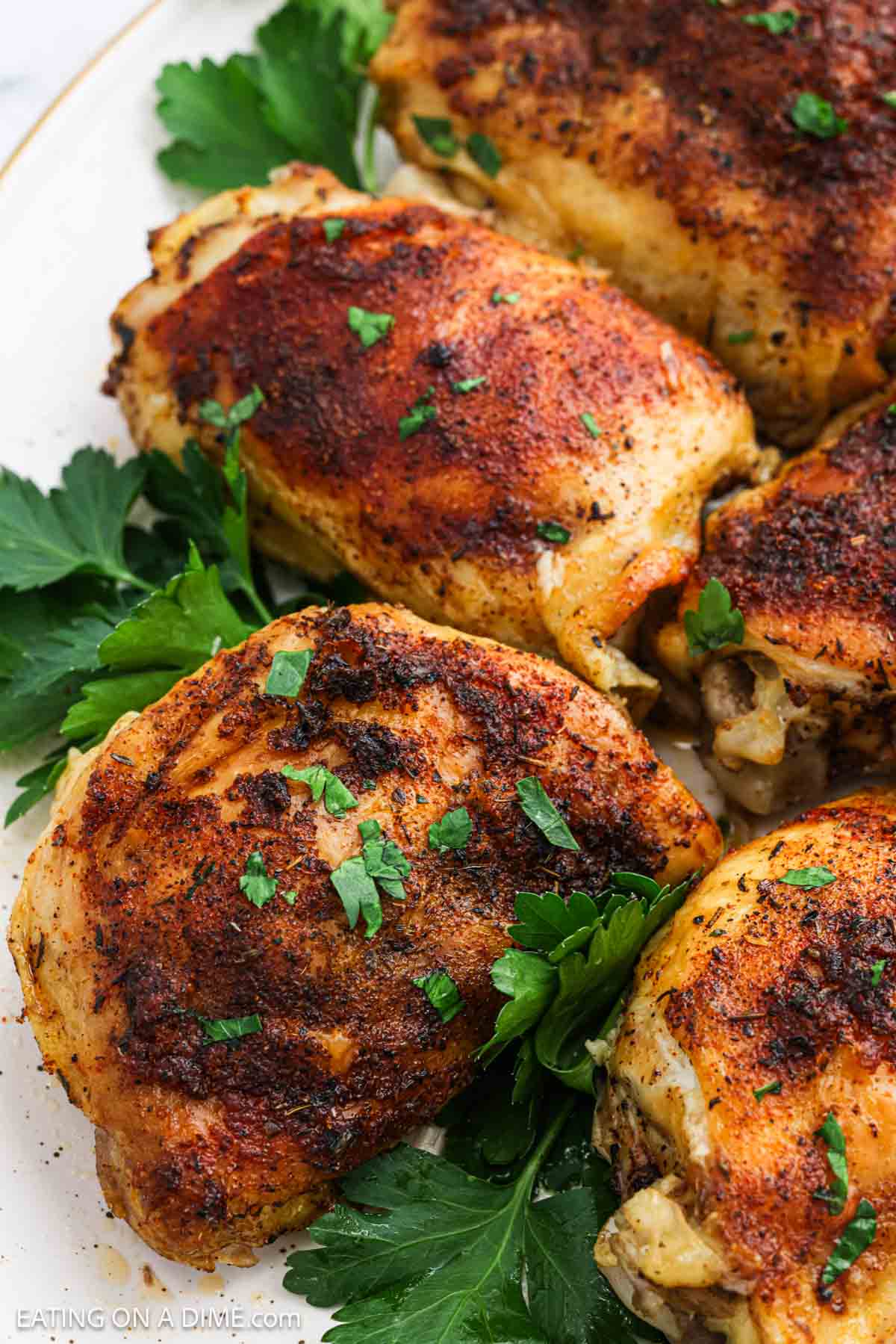 Golden brown chicken thighs on a white platter with fresh herbs on the side.