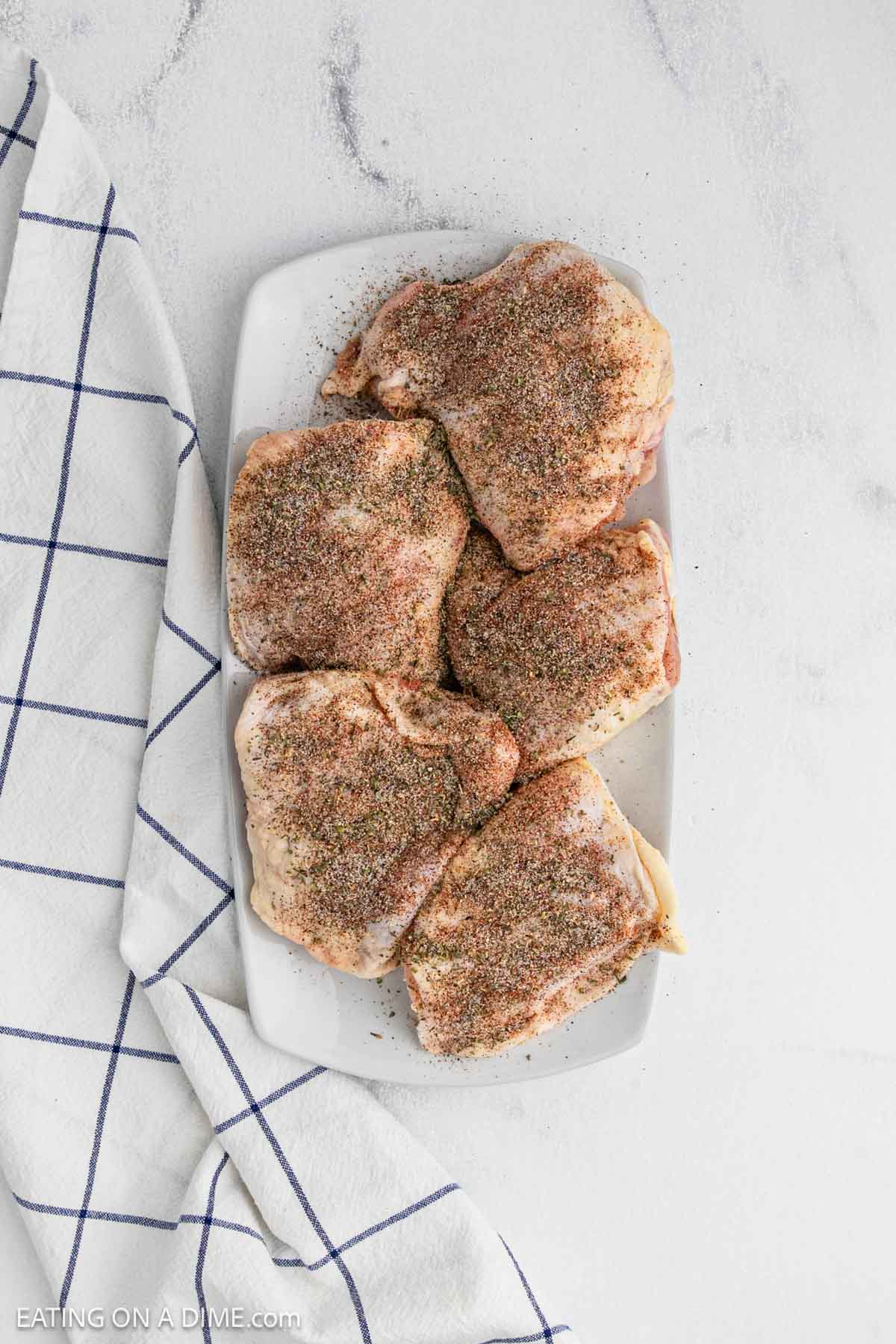Seasoned raw chicken thighs on a white platter.