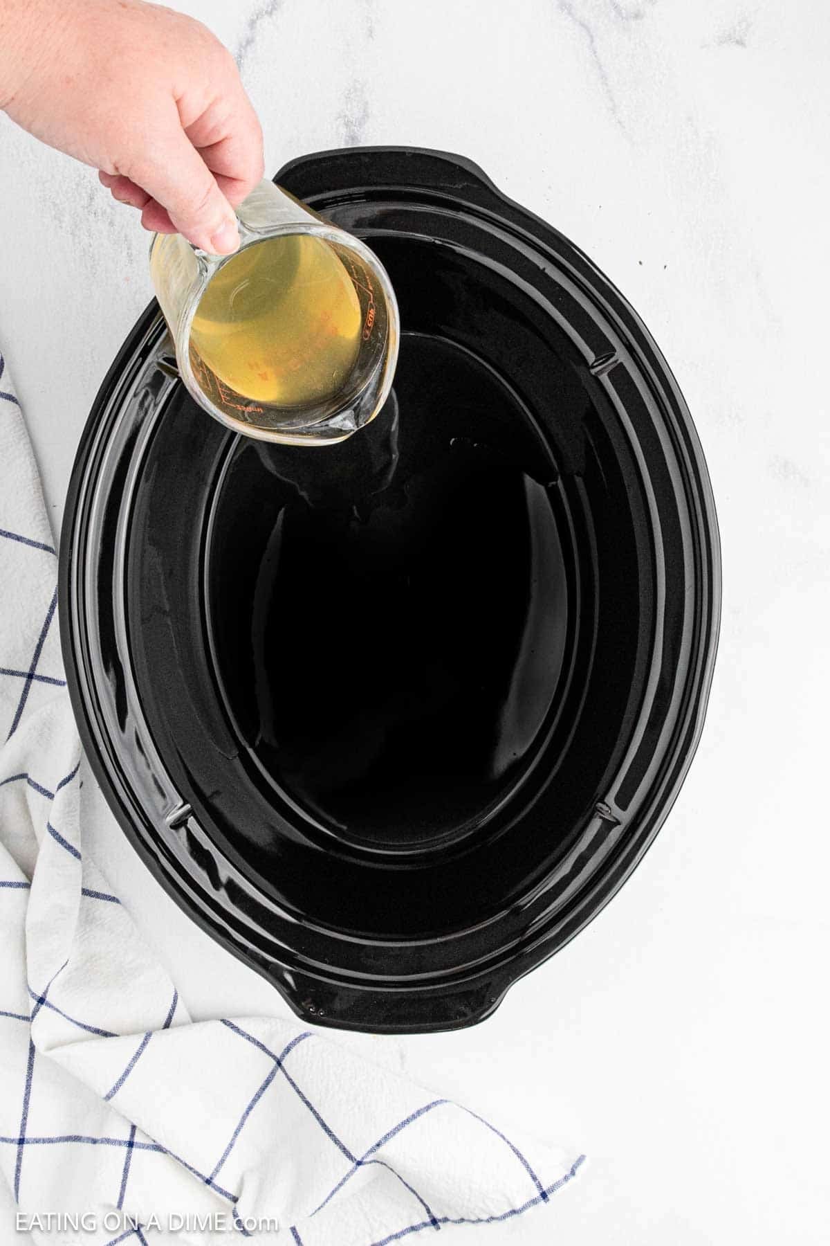 Pouring chicken brown into the black slow cooker bowl.