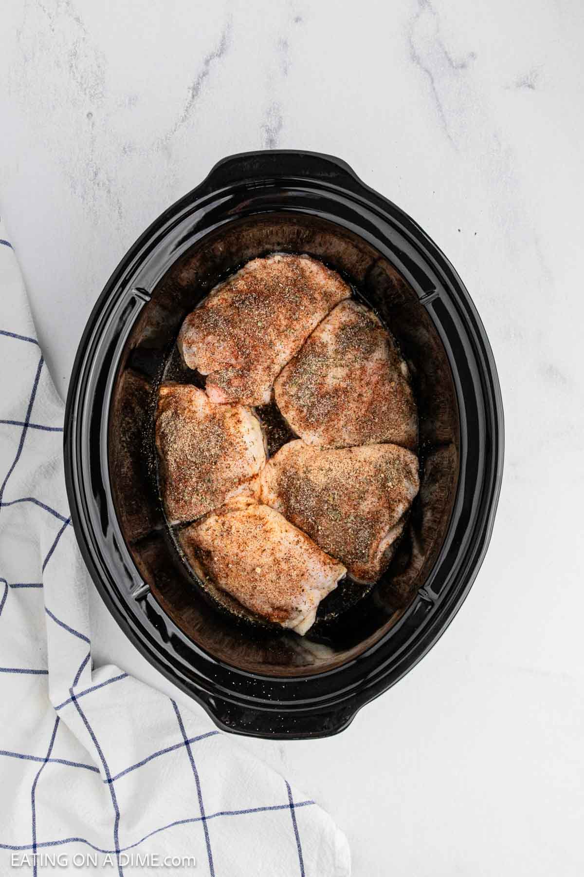 Seasoned raw chicken thighs placed in the slow cooker.