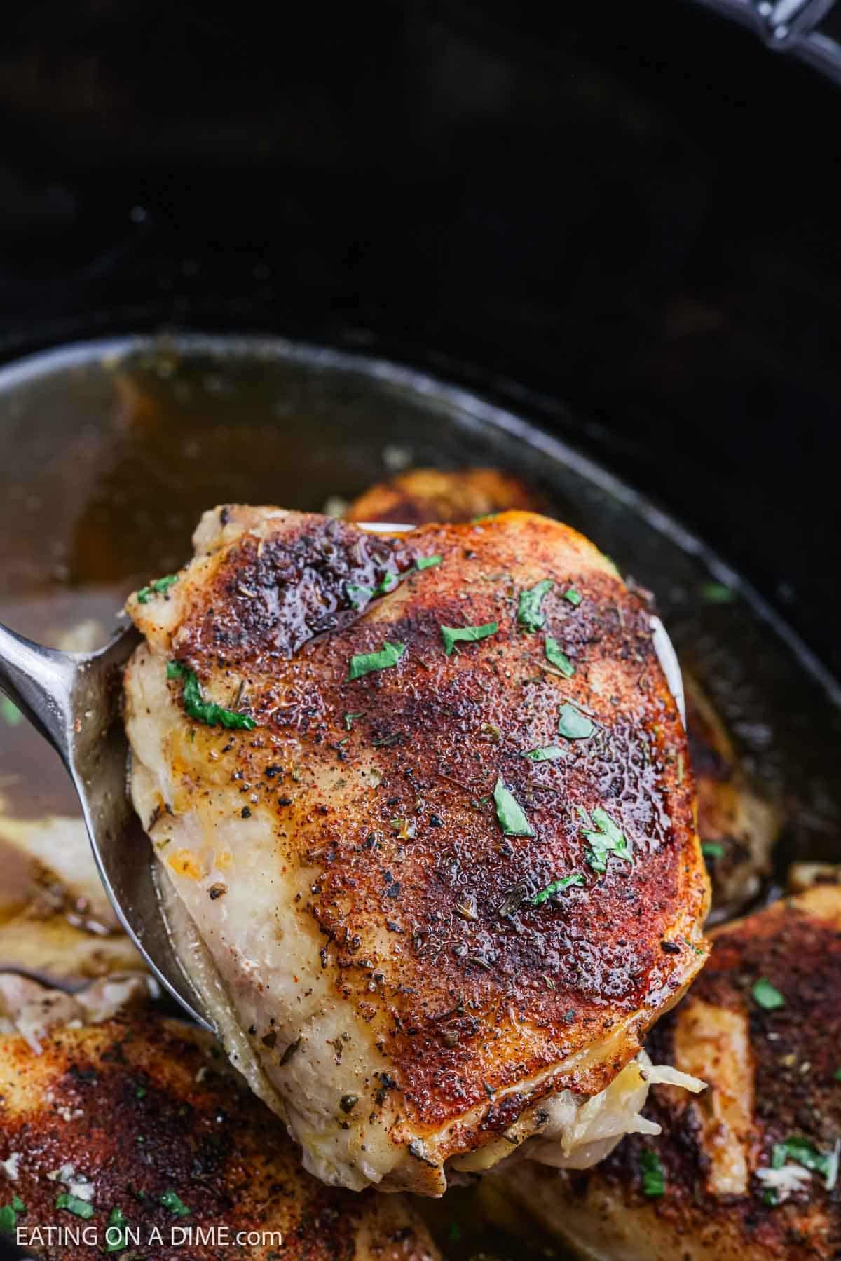 Golden Brown Chicken thighs on a spatula over a slow cooker with cooked chicken thighs in it.
