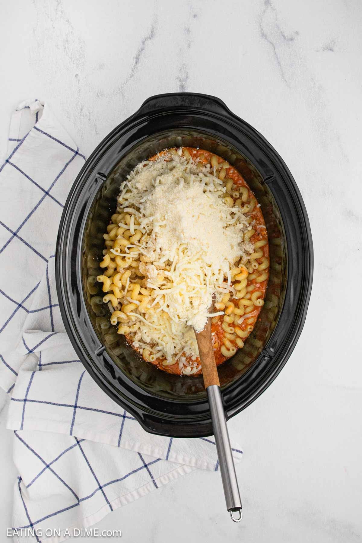 Shredded cheese, parmesan cheese, noodles, sauce in a slow cooker.
