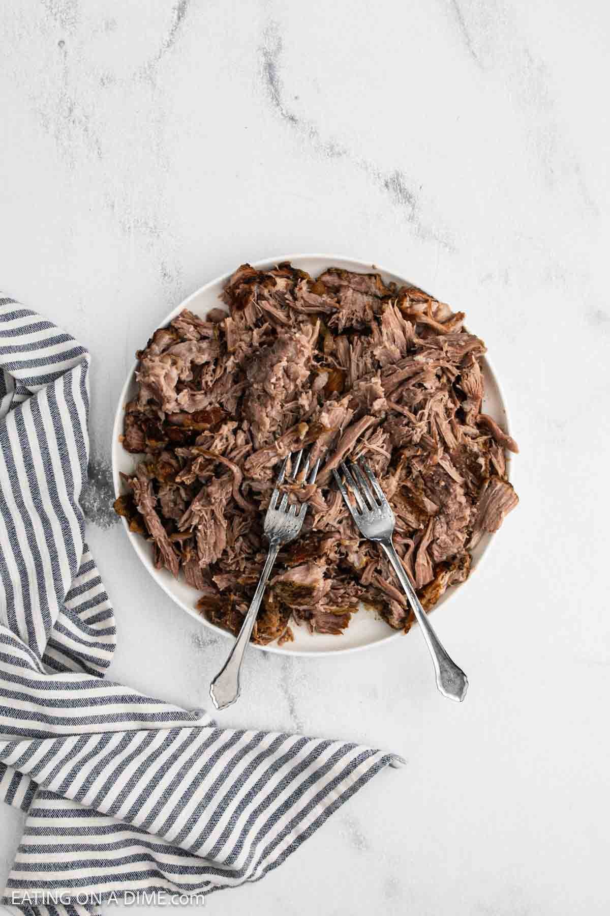 Cooked shredded pork on a plate with two fork.