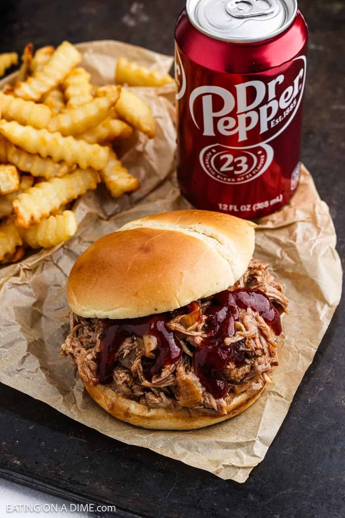 Shredded pork sandwich topped with BBQ sauce with a can of Dr Pepper and French Fries on the side.