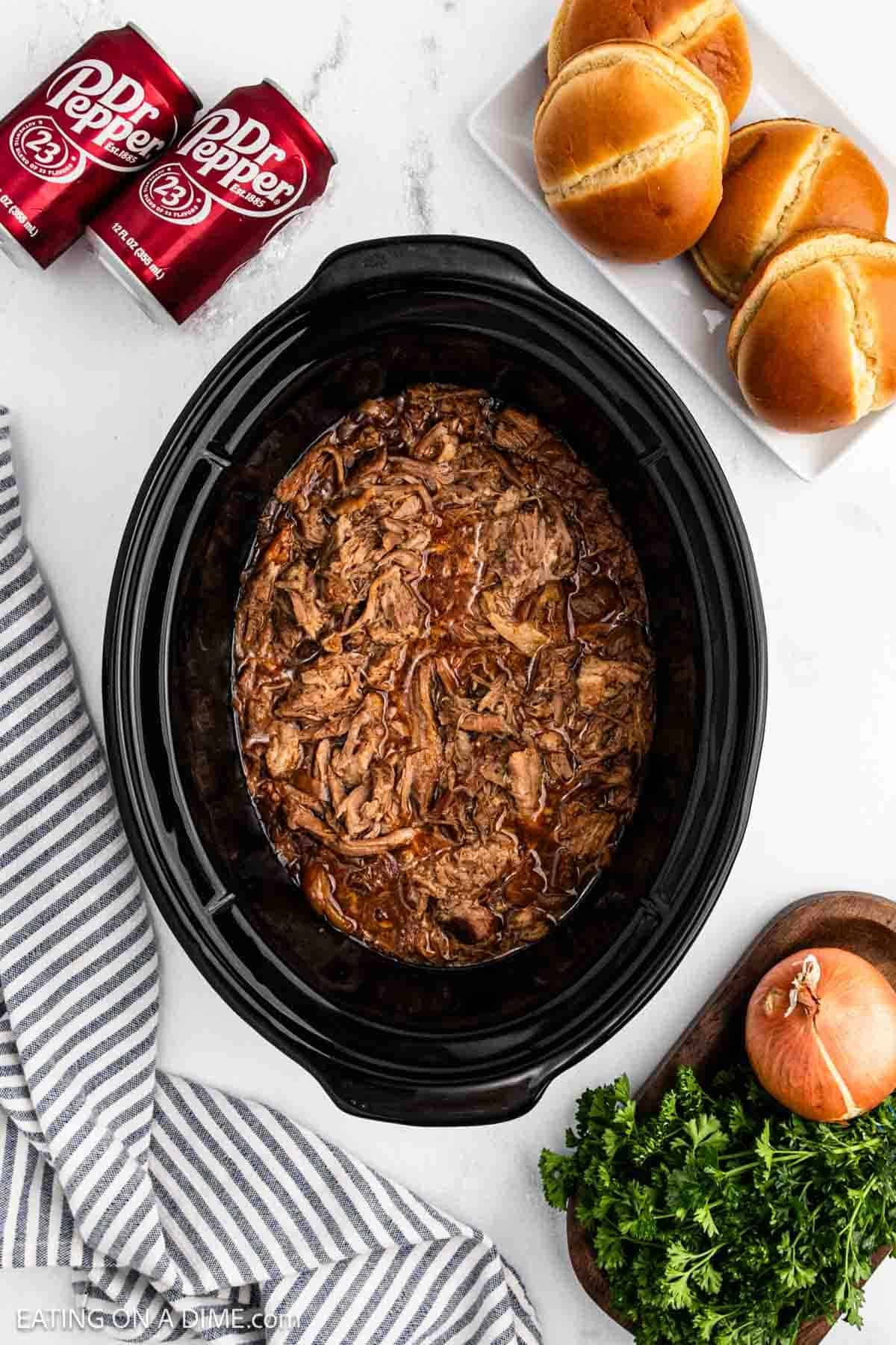 BBQ shredded pork in the crock pot with a side of hamburger buns and cans of Dr Pepper.