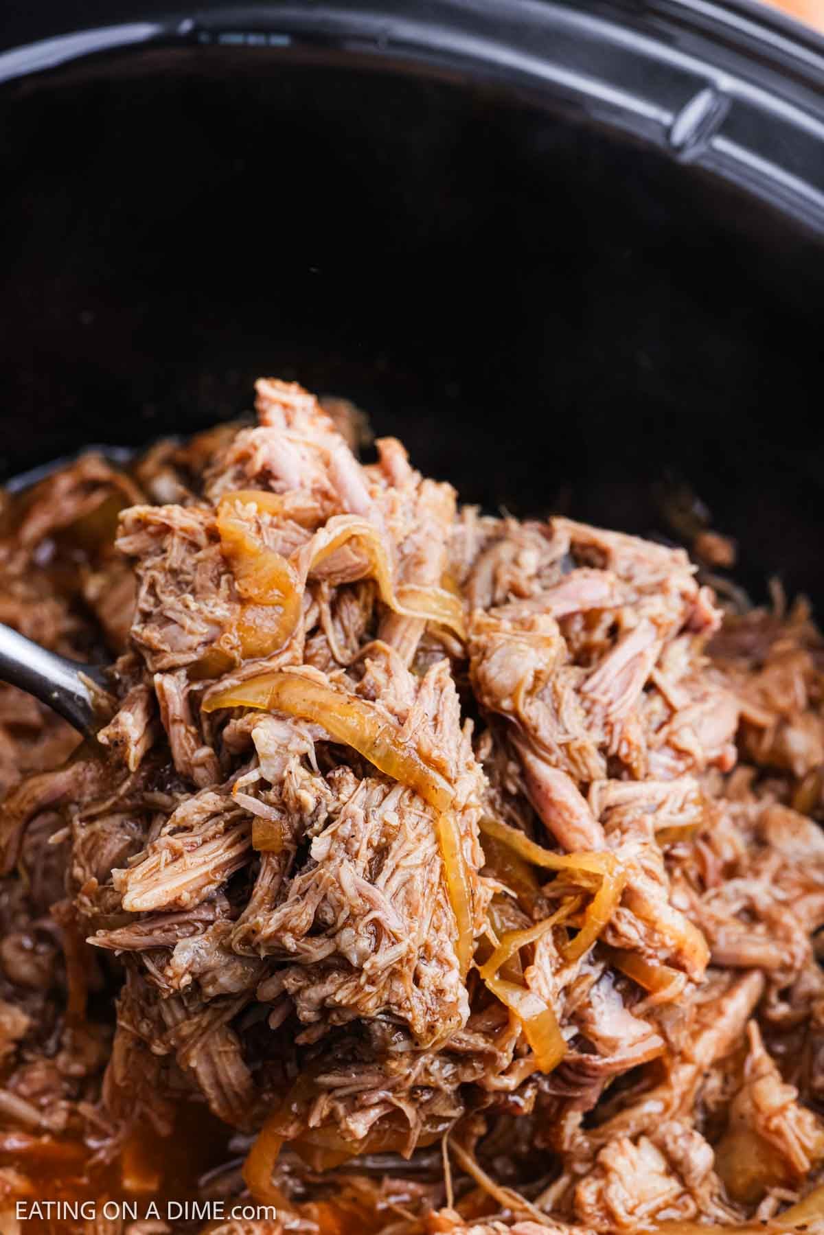 Shredded Pork in the crock pot with a serving on a spoon.