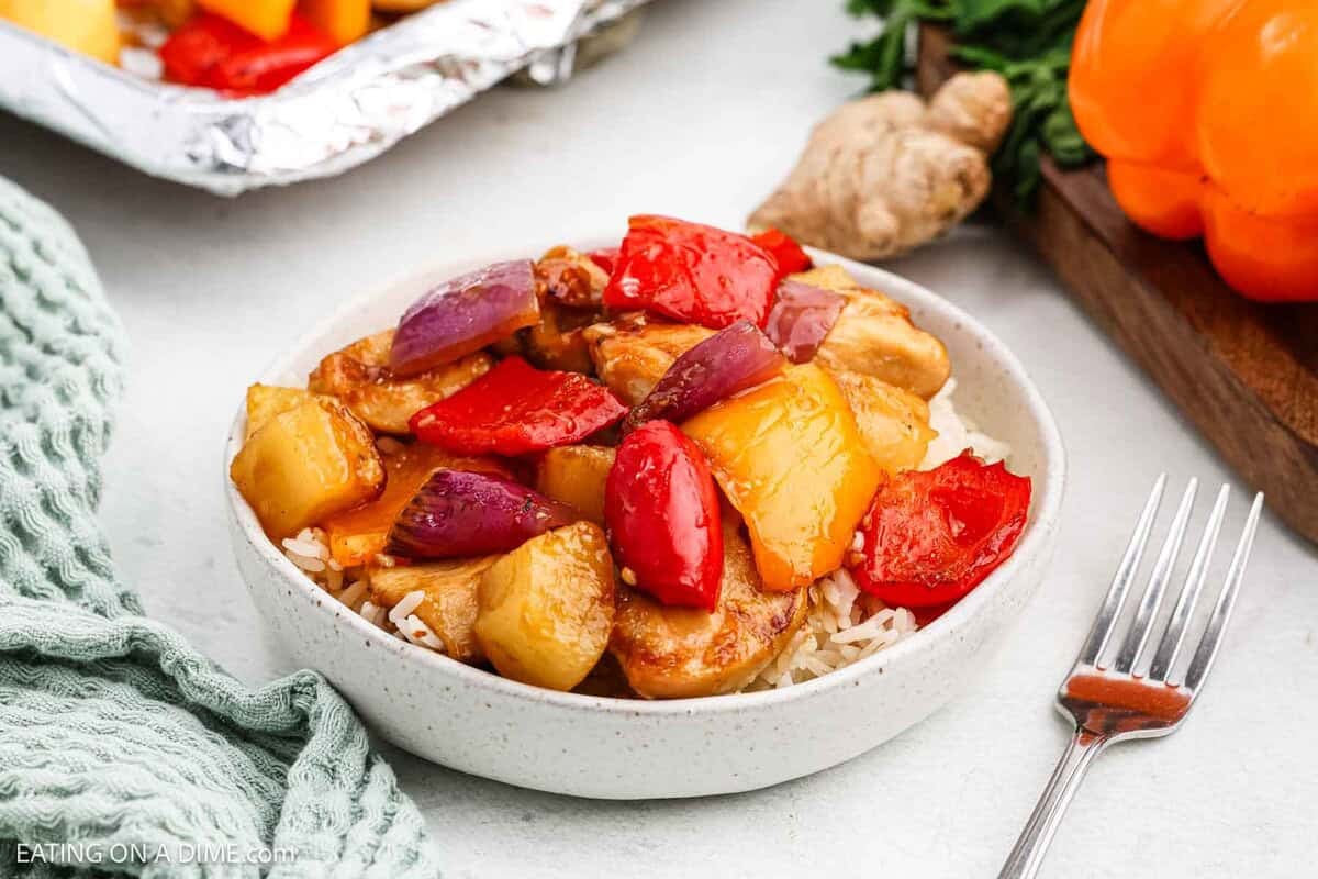 A bowl of rice topped with chunks of Hawaiian Chicken, pineapple, red and yellow bell peppers, and red onions in a savory sauce.