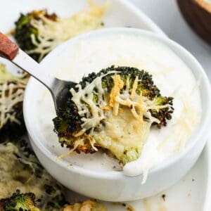 A serving of smashed broccoli being dipped into a bowl of ranch.