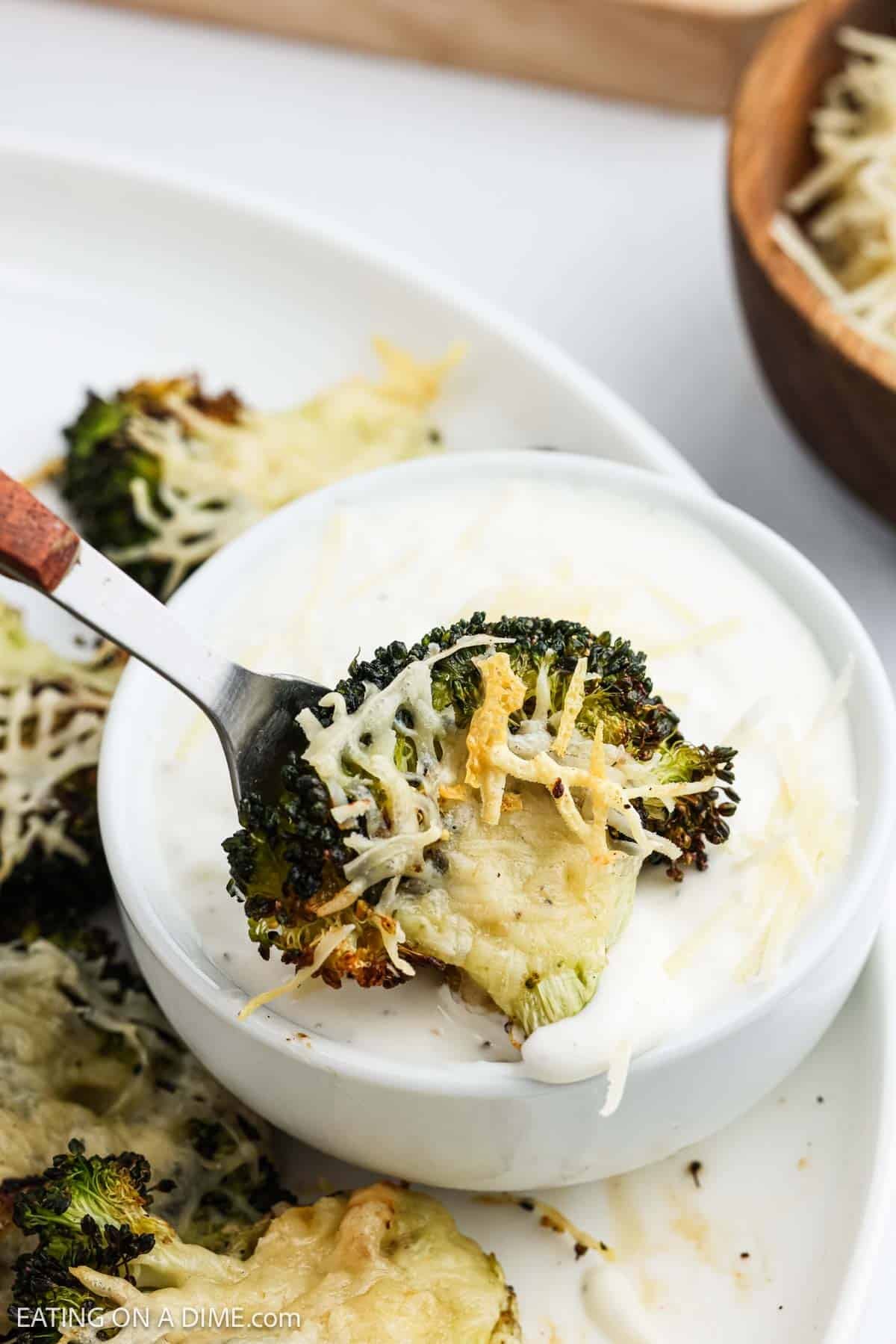 A serving of roasted broccoli topped with melted cheese being dipped into ranch dressing with a fork.