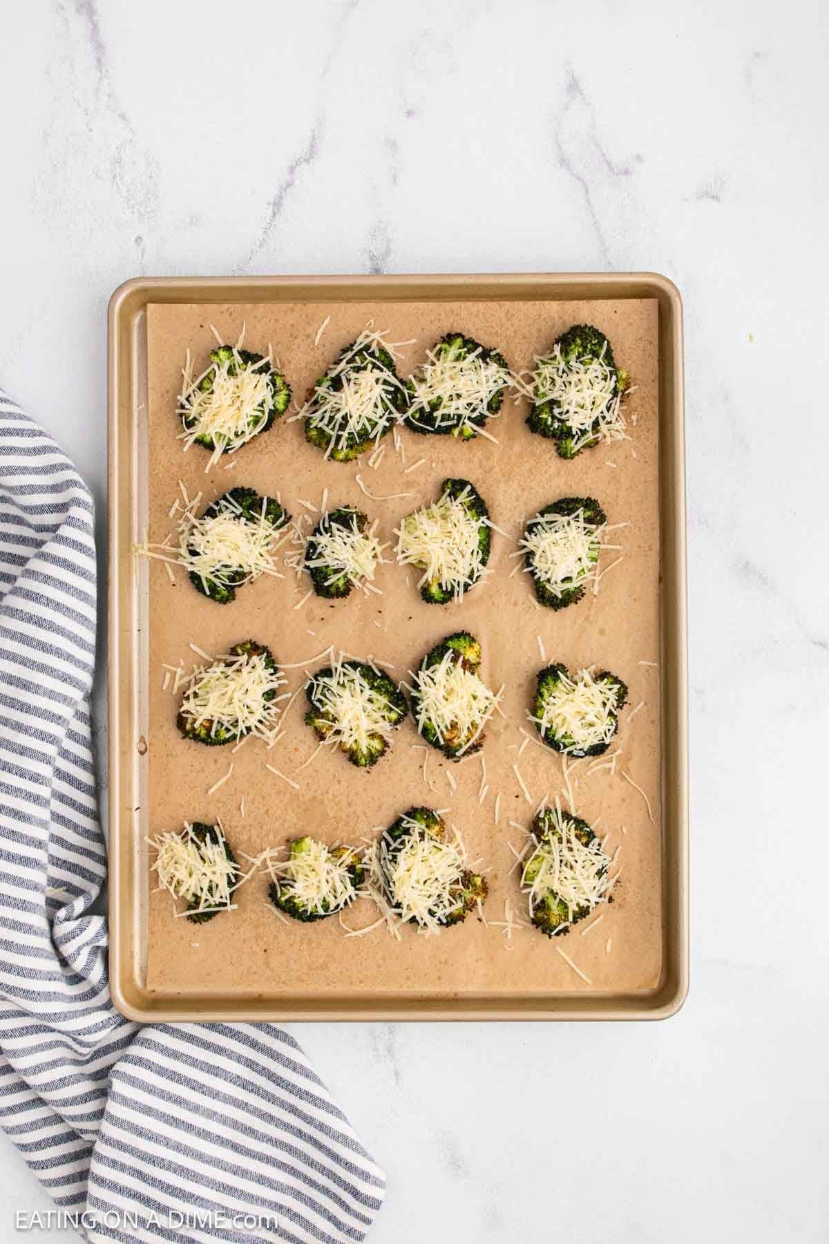 Roasted broccoli topped with shredded parmesan cheese on a baking sheet lined with parchment paper.
