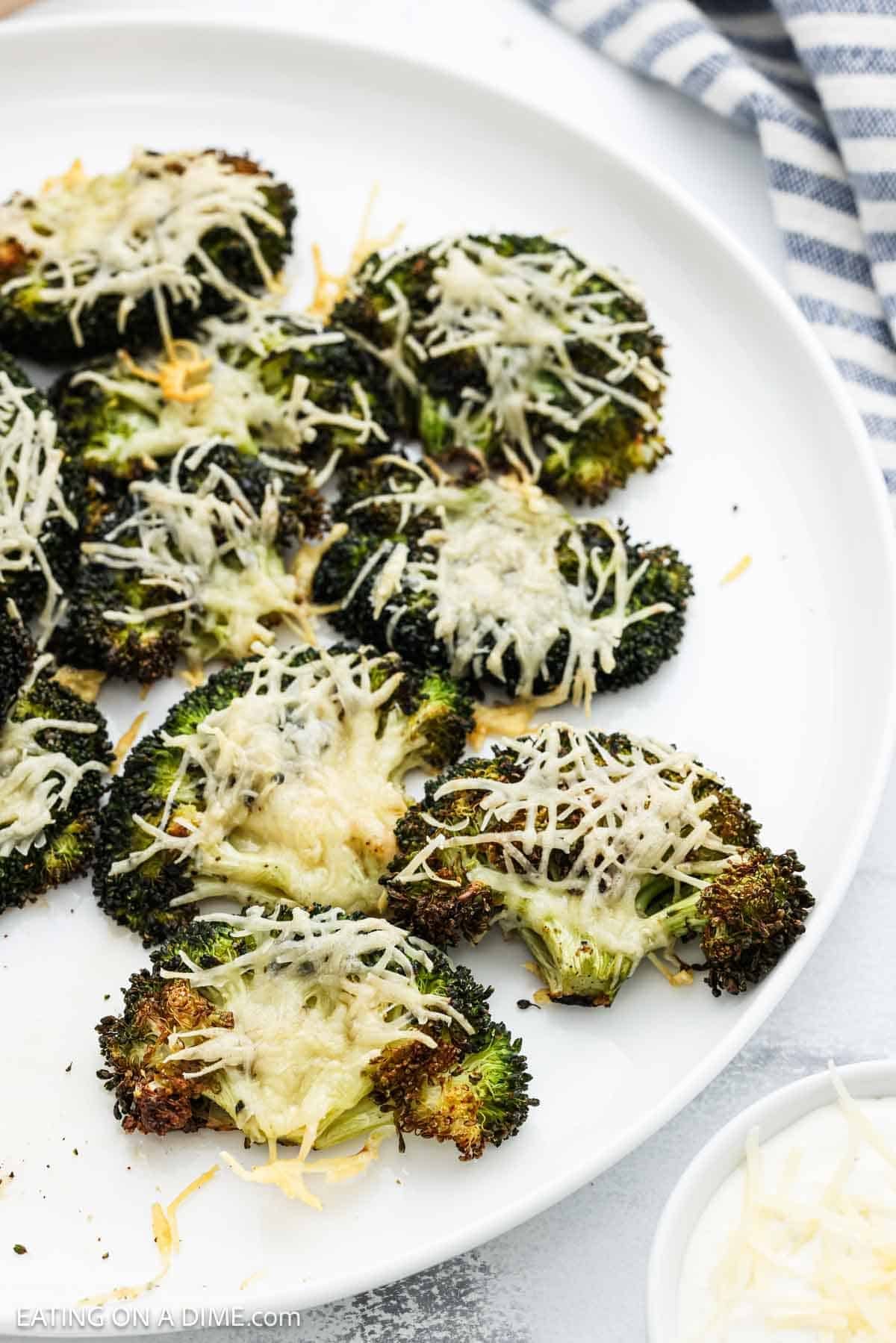 Roasted broccoli on a white platter topped with melted parmesan cheese.