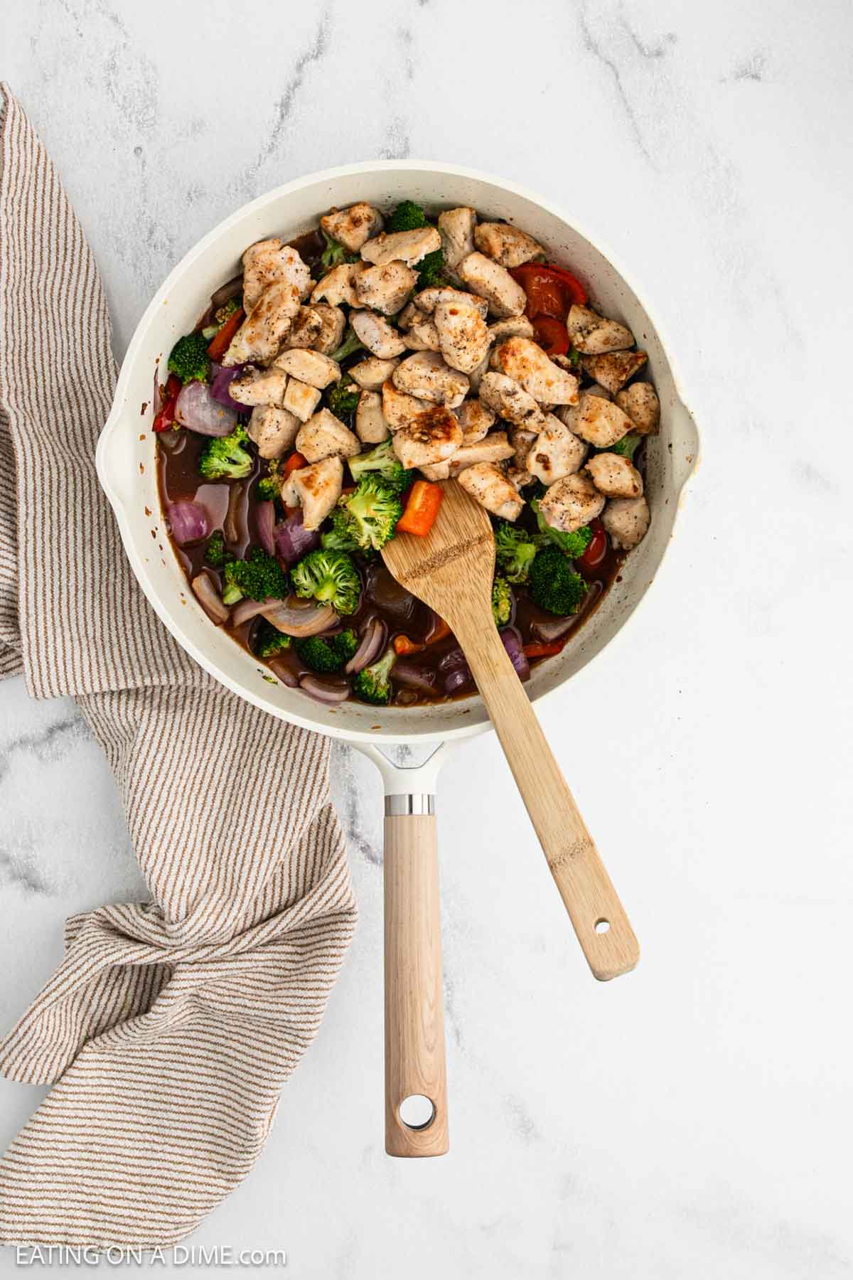 Cooked diced chicken in a skillet with cooked red onion, bell pepper and broccoli covered in sauce.