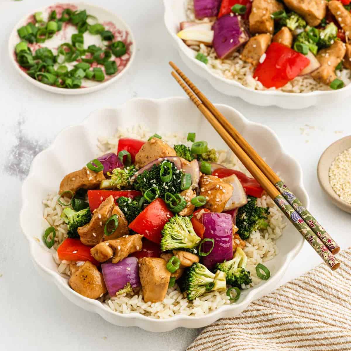 Teriyaki Chicken with fresh veggies over rice in a bowl with chopsticks on the side.