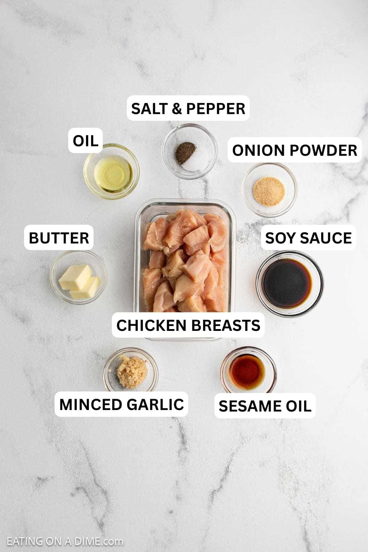 Hibachi Chicken Ingredients - small bowls of minced garlic, sesame oil, soy sauce, butter, onion powder, salt, pepper, and oil with a diced chicken breast in a clear container