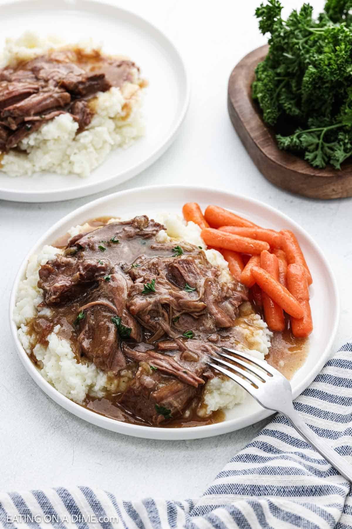 A serving of the roast and gravy over mashed potatoes with a side of carrots on a plate.