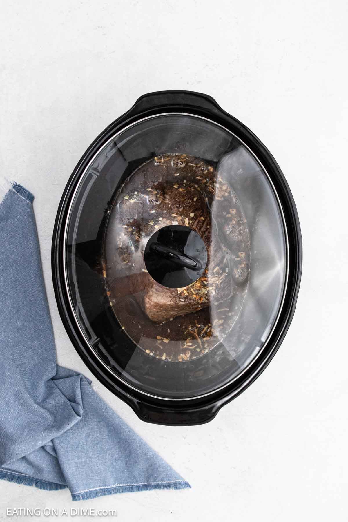 Lid covering the slow cooker with the roast ingredients inside.
