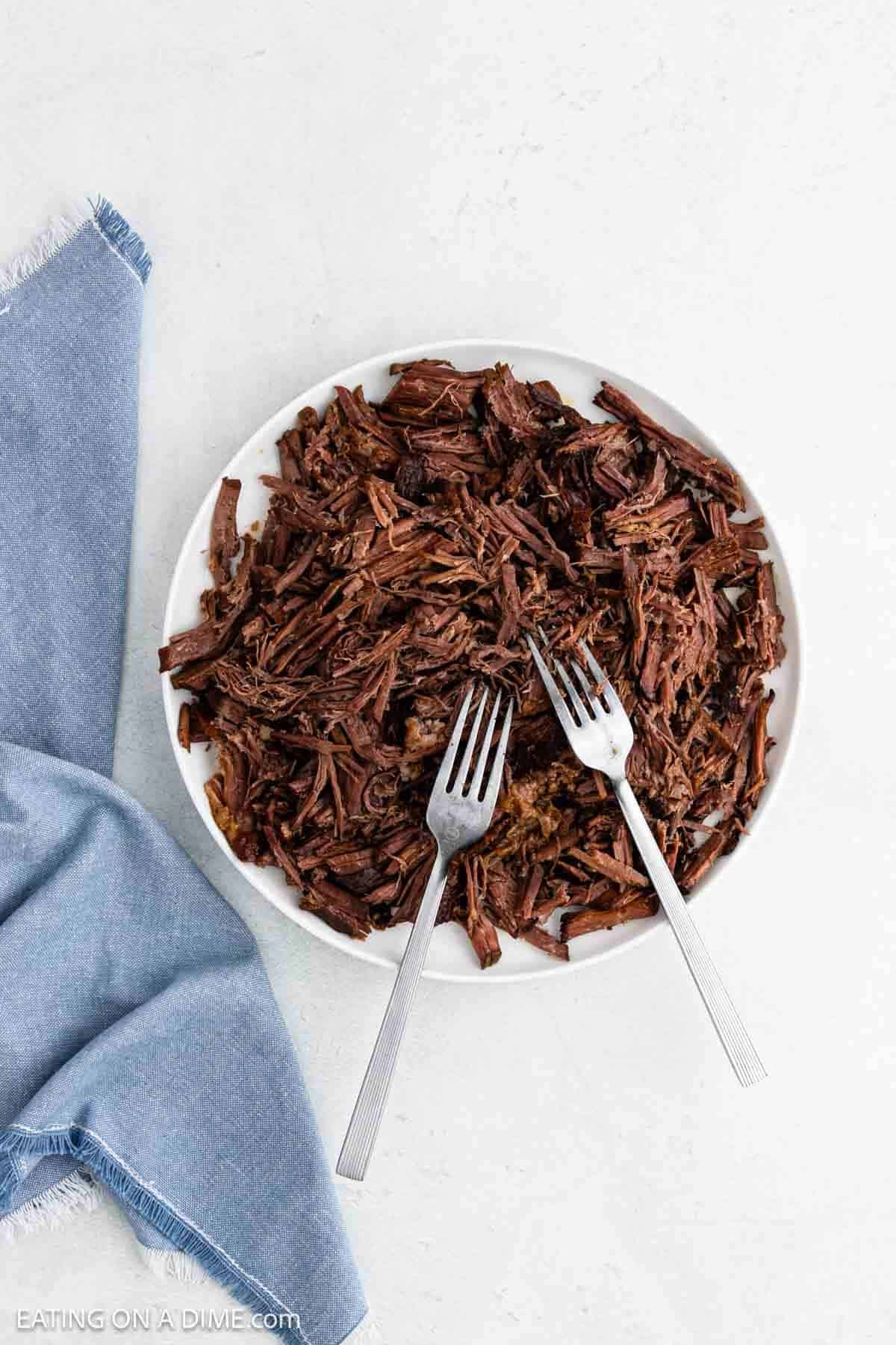 Shredding the roast on a plate with two forks.