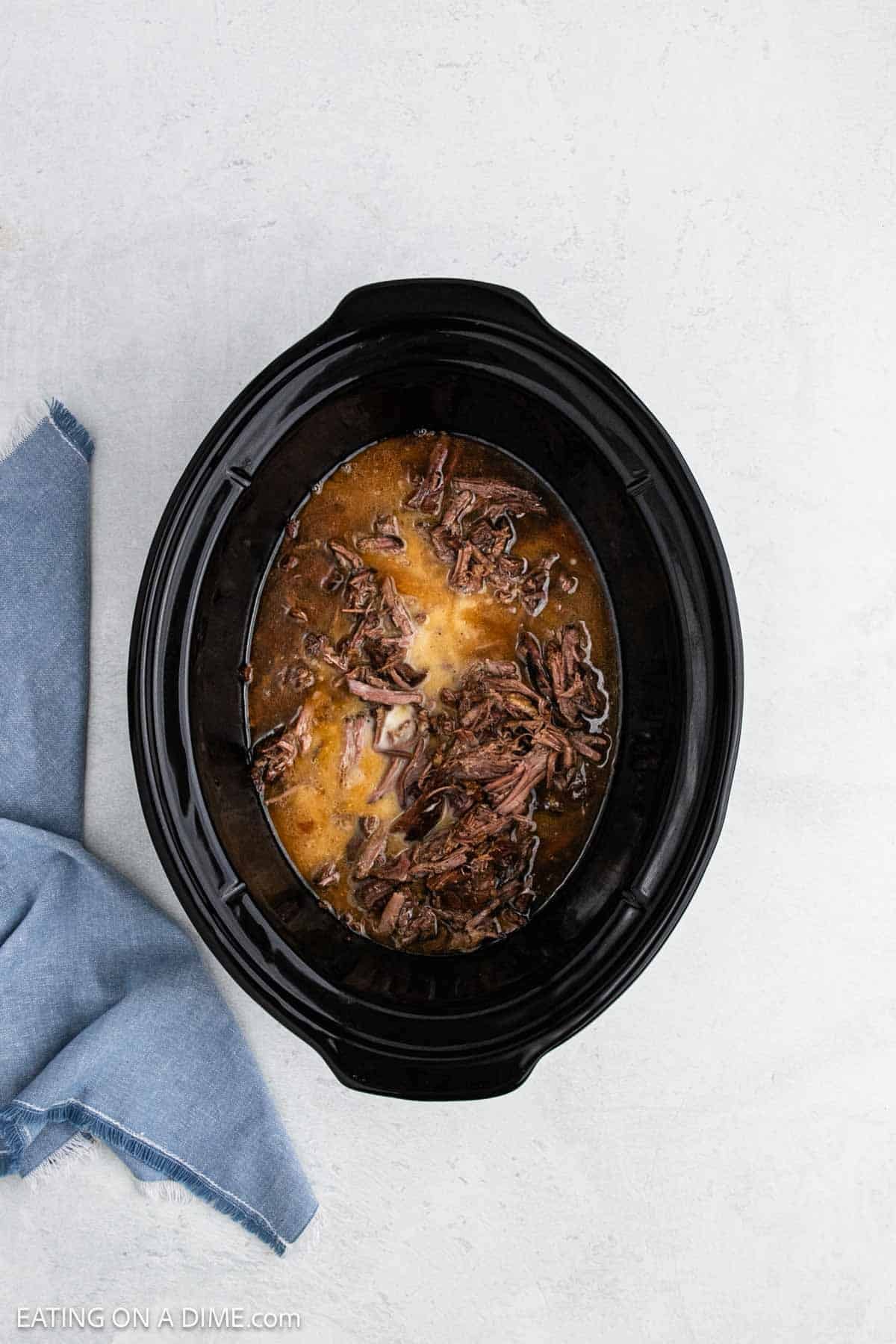 Shredded beef in the slow cooker topped with cornstarch mixture.